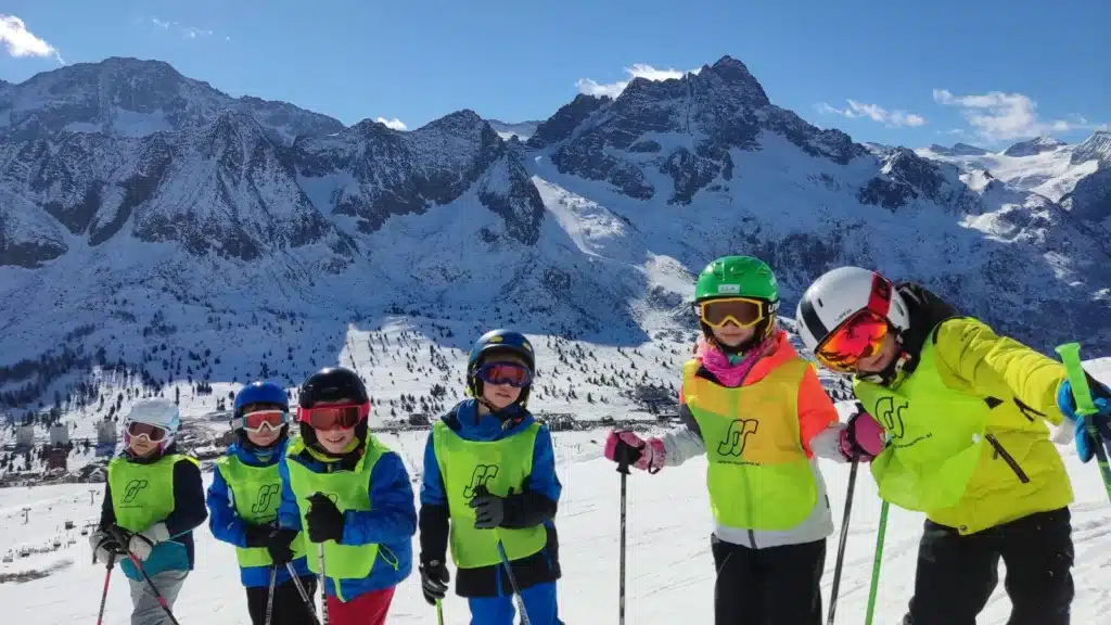 Nasmejani otroci v jopičih SnowSun na smučišču z mogočnimi zasneženimi alpskimi vrhovi v ozadju