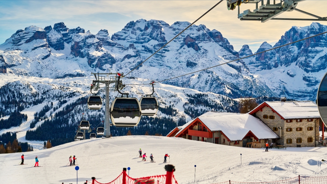 Smučarji na zasneženih progah z gondolo in alpskimi kočami pod dolomitskimi vrhovi – smučanje Dolomiti v največjem smučarskem območju na svetu.