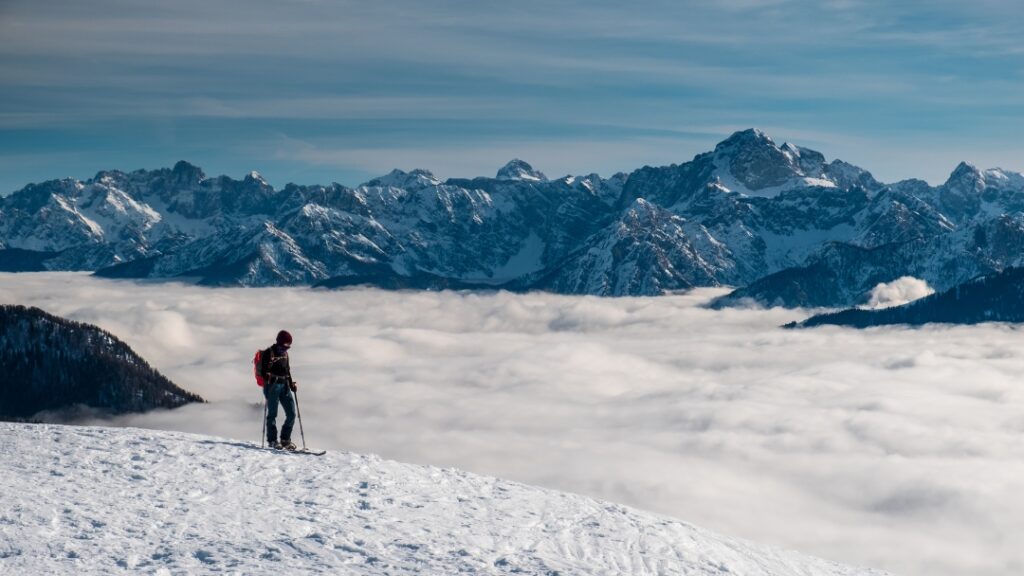 Smučarka na snegu s pogledom na zasnežene alpe in oblačno dolino - zimski gorski turizem in alpinizem v Furlanjiji.