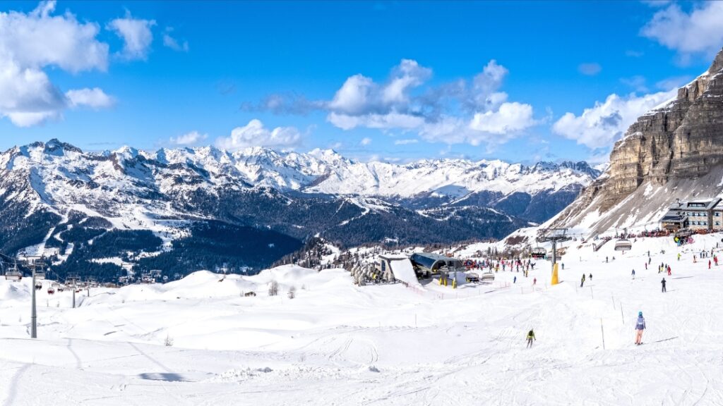 Panoramski pogled na smučišče Trentino s smučarji, žičnicami in zasneženimi dolomitskimi vrhovi – vodnik za zimske počitnice v zahodni Italiji.
