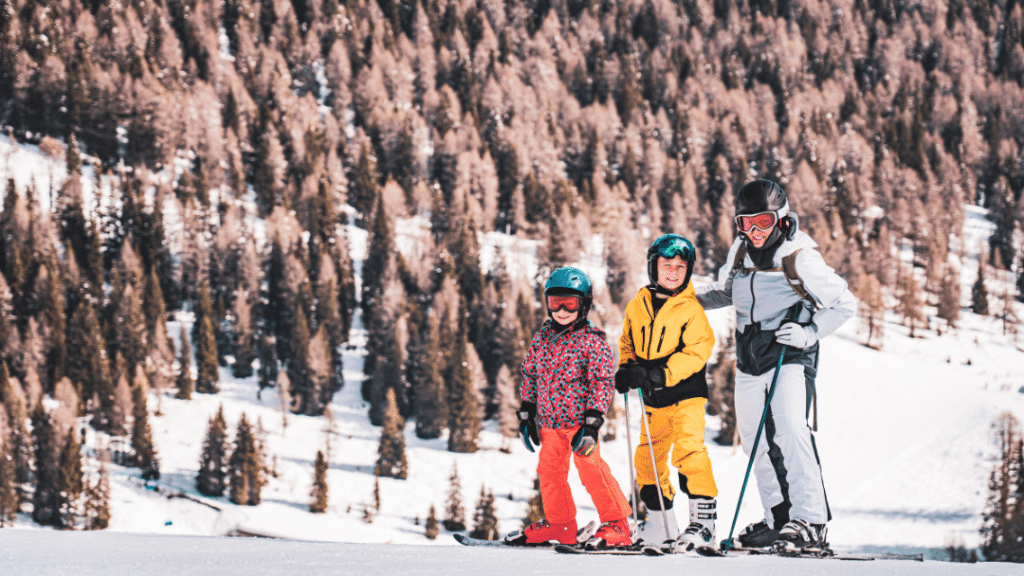 Družina smučarjev na zasneženi progi v Italiji z gozdnatim ozadjem prikazuje ceno smučanja in dejavnike ki vplivajo na stroške zimskih počitnic v italijanskih Alpah 2026