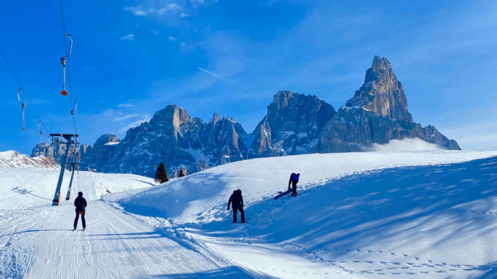 Smučarji na urejeni progi v Trentinu z dramtičnimi dolomitskimi vrhovi, realen pregled stroškov smučanja 2026..